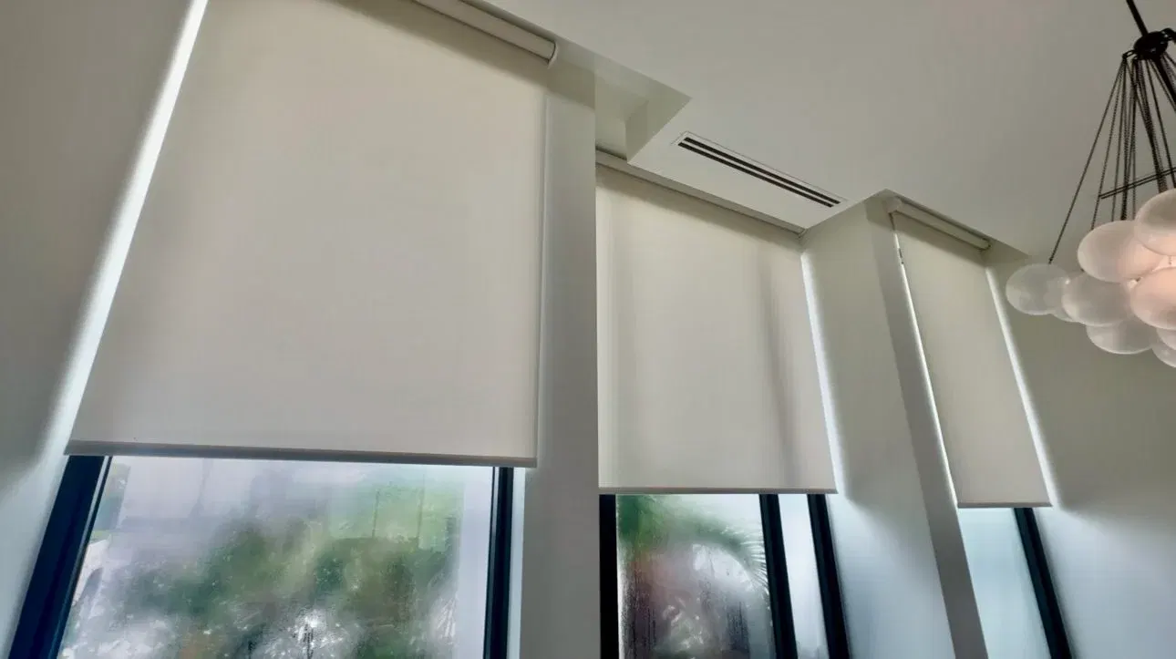 Motorized solar shades lowering in sync from recessed ceiling pockets across a wall of west-facing windows in a St. Louis great room at golden hour